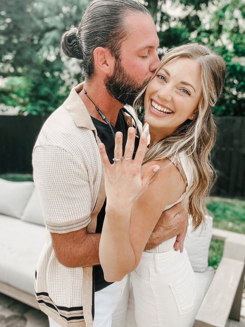 Man holding woman kissing side of face holding up engagement ring 