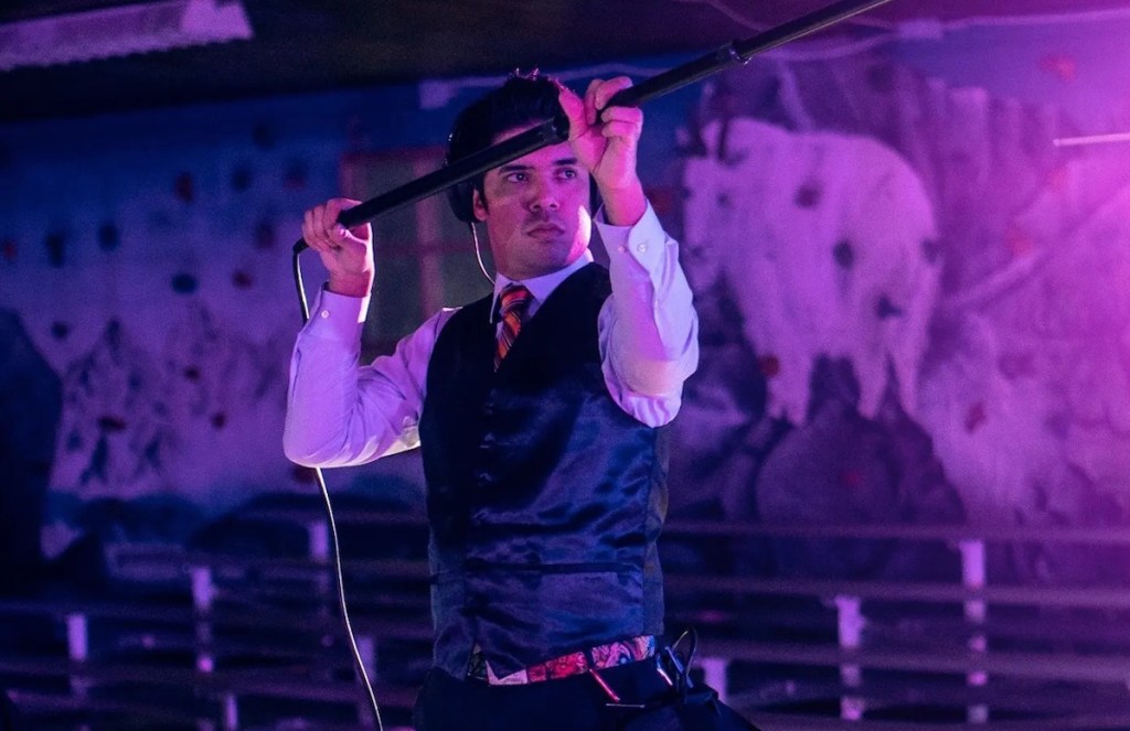 man in purple dark room holding pole for filmmaking
