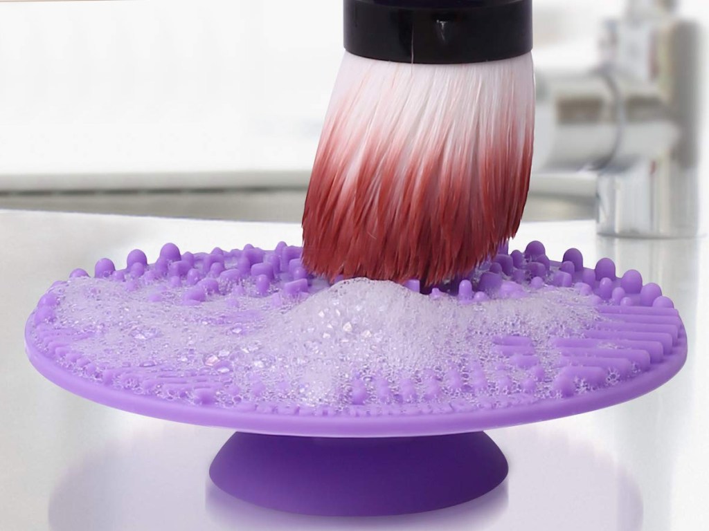 cleaning a makeup brush on a purple silicone pad