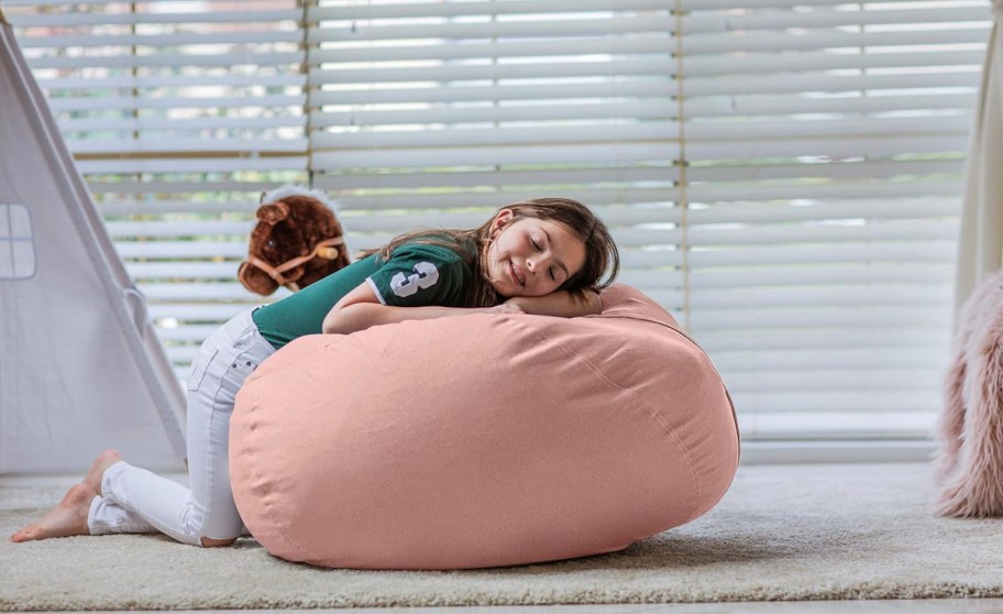 girl laying on top of pink bean bag chair on floor in bedroom