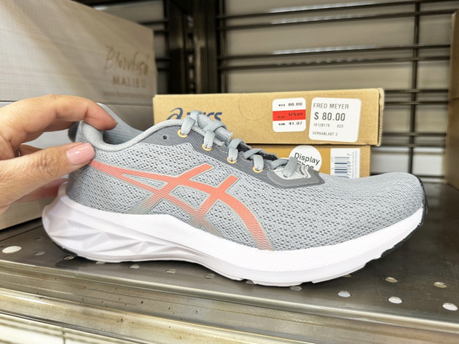 hand touching light grey and pink asics running shoe on store display shelf