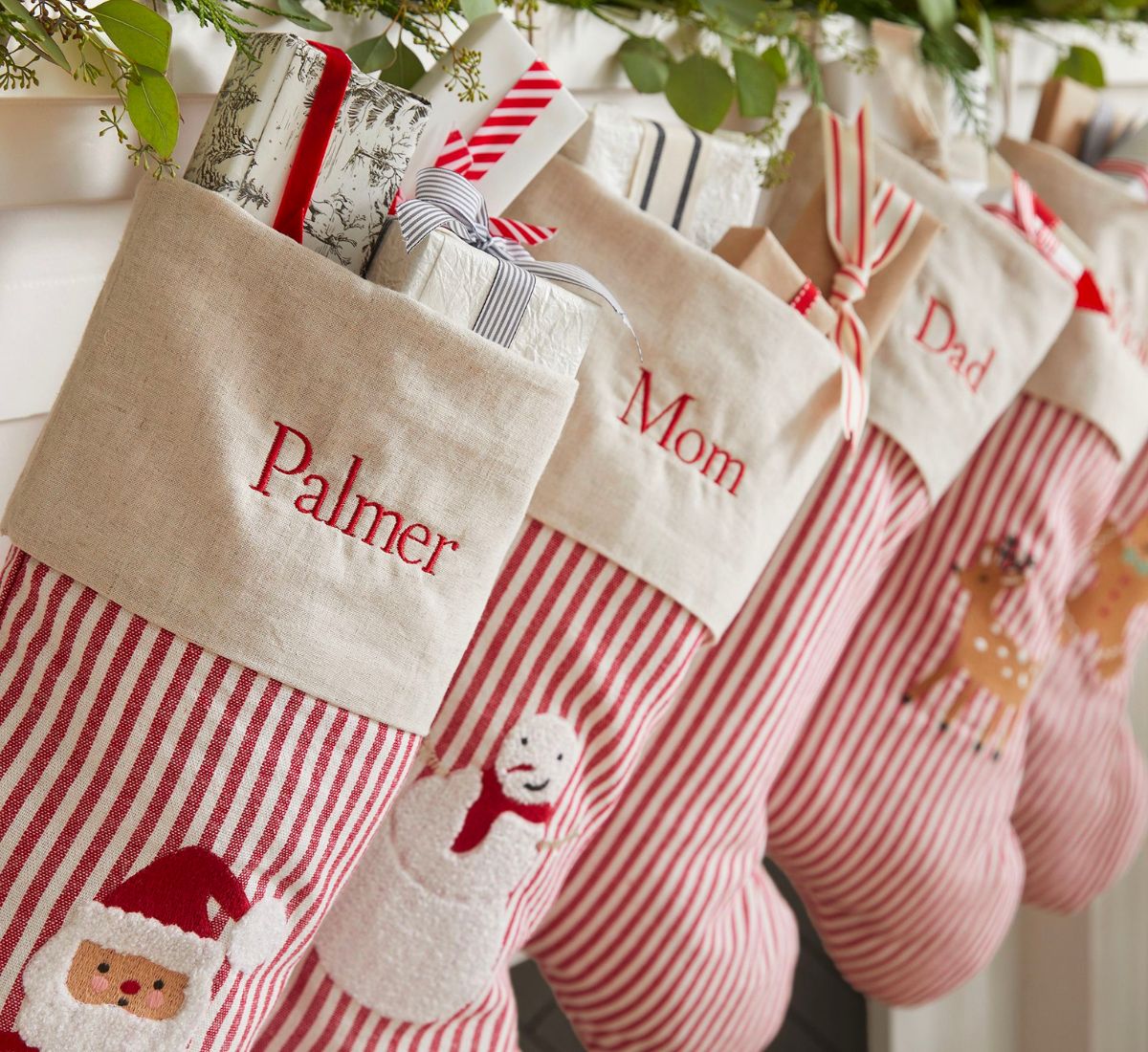 five Gingerbread Ticking Stripe Christmas Stockings hanging on a white wooden fireplace mantle decorated with green garland