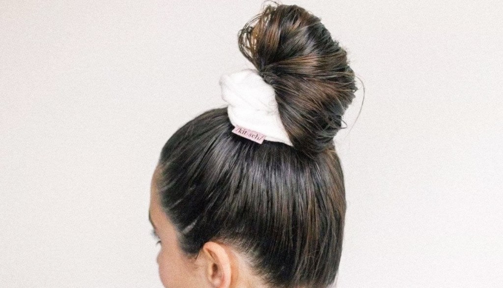 woman with dark brown hair up in a bun with white scrunchie