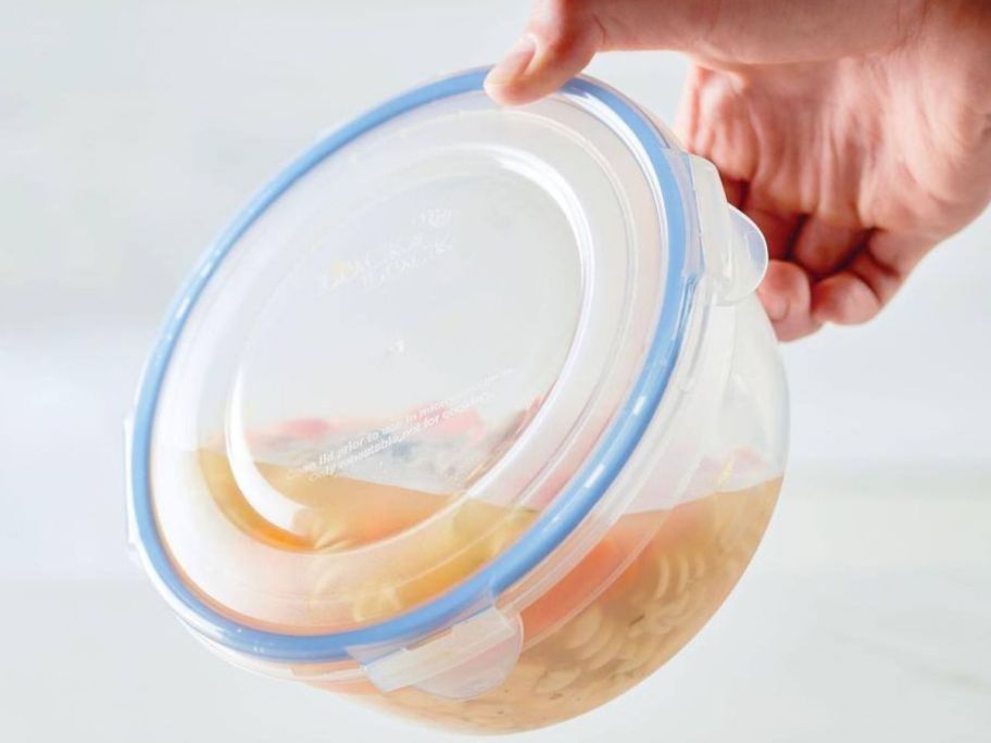 Hand tipping a closed lock n lock round storage bowl filled with chicken noodle soup to show how it's leakproof