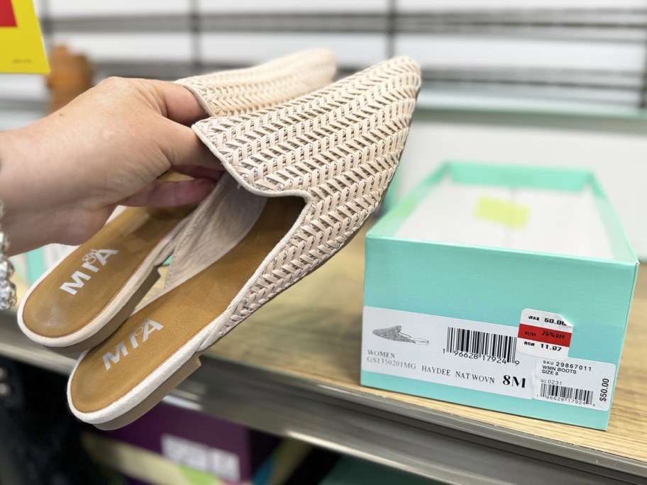 hand holding pair of shoes above their shoe box on store display rack