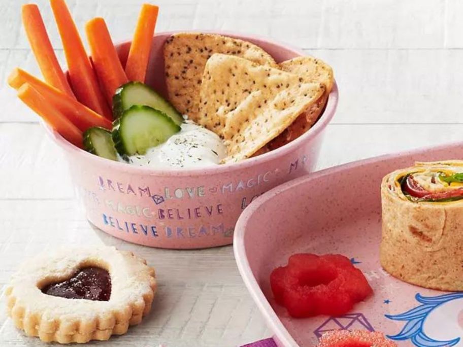 Close up view of Member's Mark kids dinnerware bowl filled with veggies and crackers and a plate with ketchup and a roll-up sandwich on it