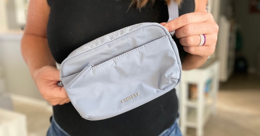 woman holding a grey Athleta belt bag up to the camera