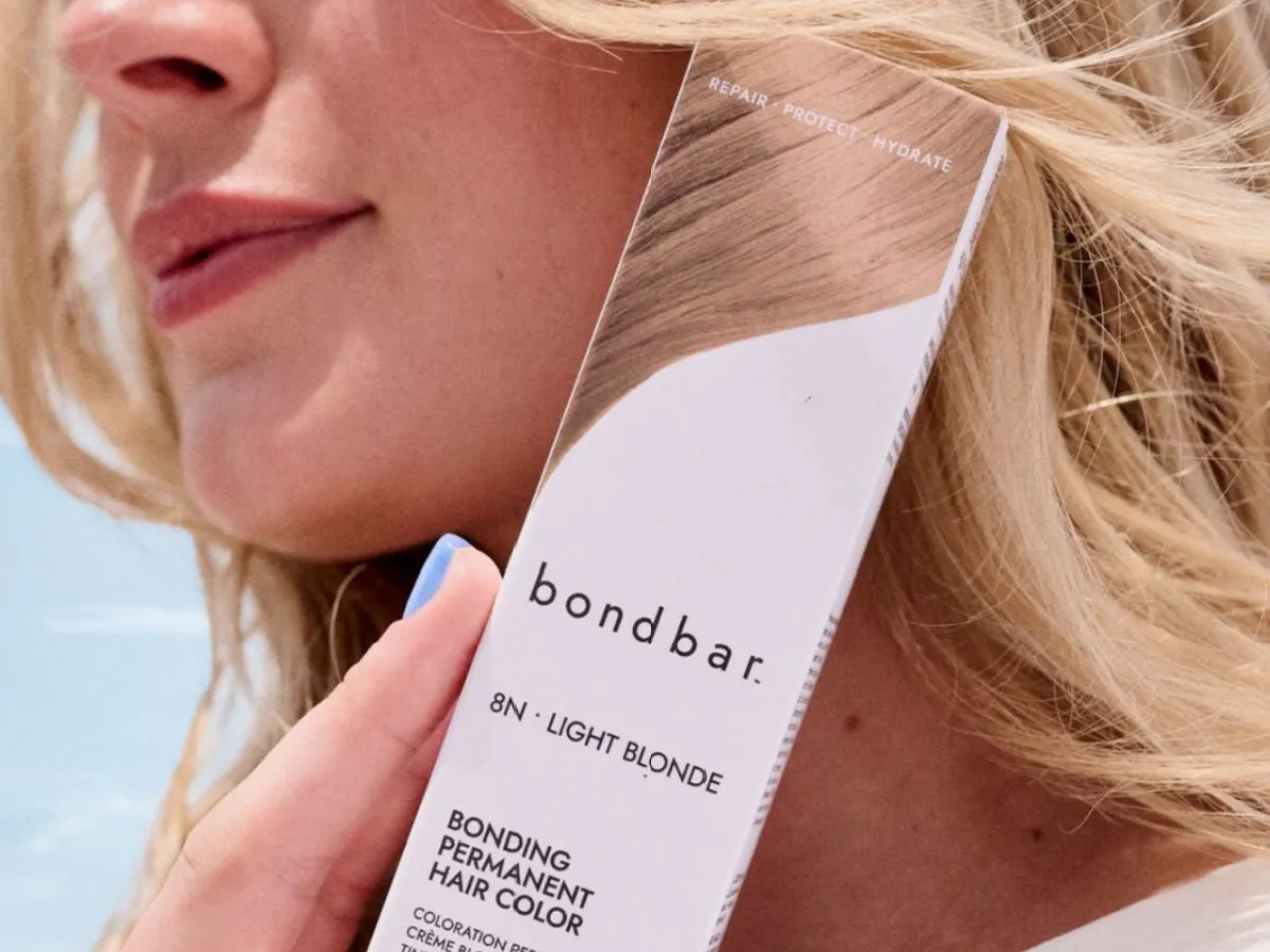 smiling woman with blonde hair holding a sally hansen bondbar hair color box near her face