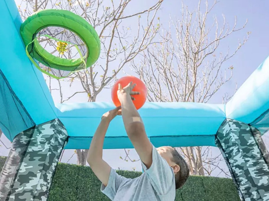 boy throwing basketball into hoop in bounce house