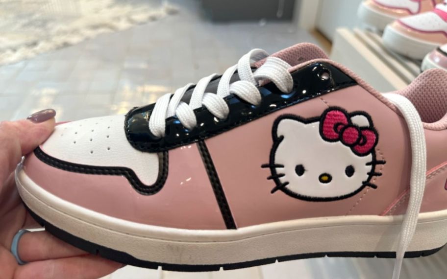 a womans hand holding a pink hello kitty sneaker