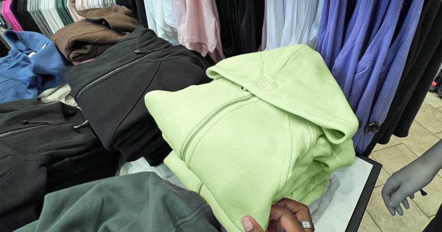 hand touching folded stack of lululemon scuba hoodies in store