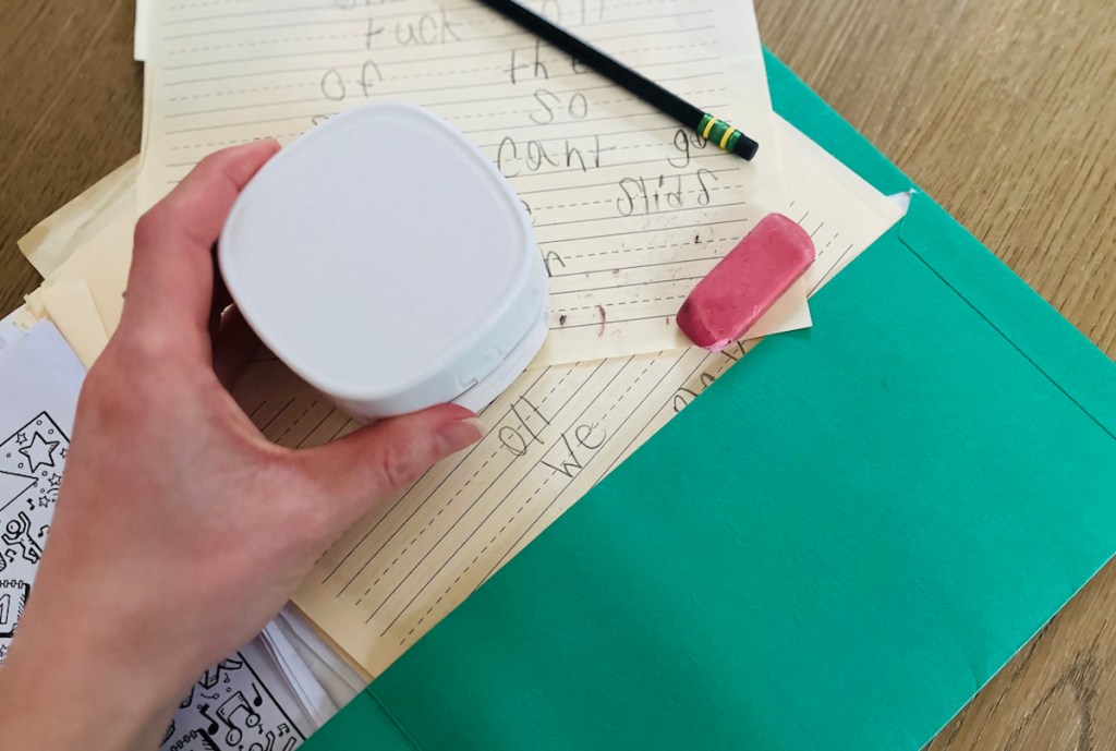 hand holding white mini desk vacuum over green notebook with eraser shavings