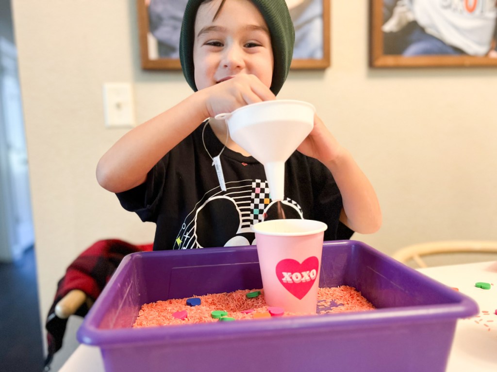 kid holding funnel playing w/ sensory bin