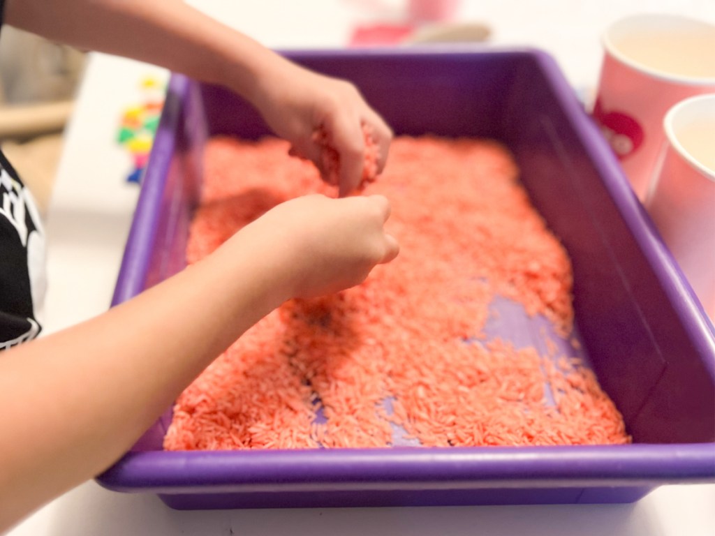 hands grabbing pink rice in bin