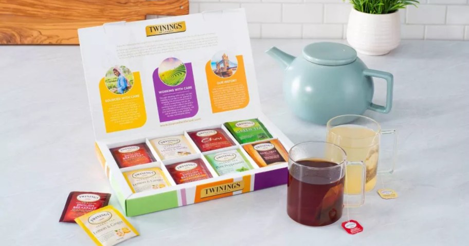 box of assorted tea bags next to mugs and kettle