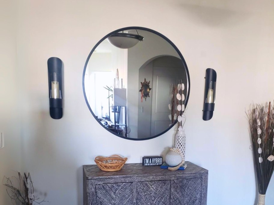 a large round wall mirror above a entryway table with decor