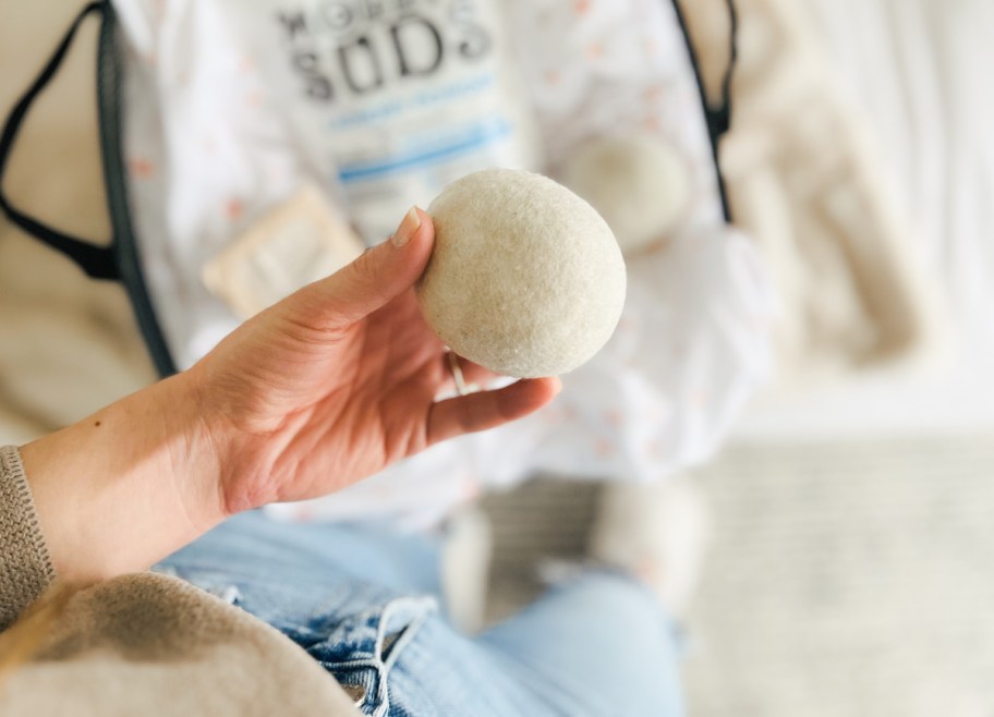 hand holding a white wool dryer ball over laundry detergent