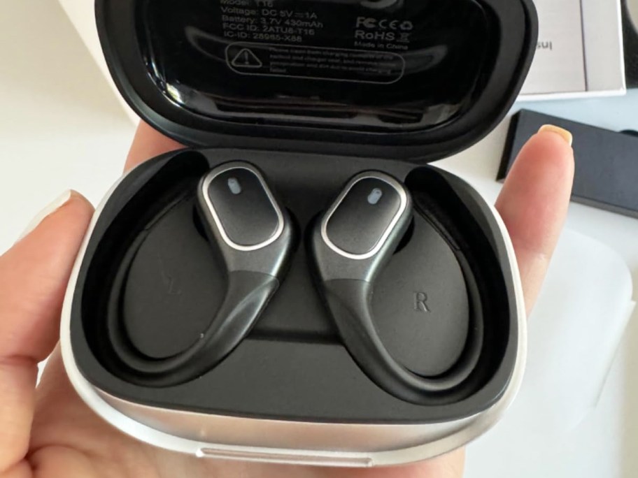 hand holding a set of black bluetooth headphones in their charging case