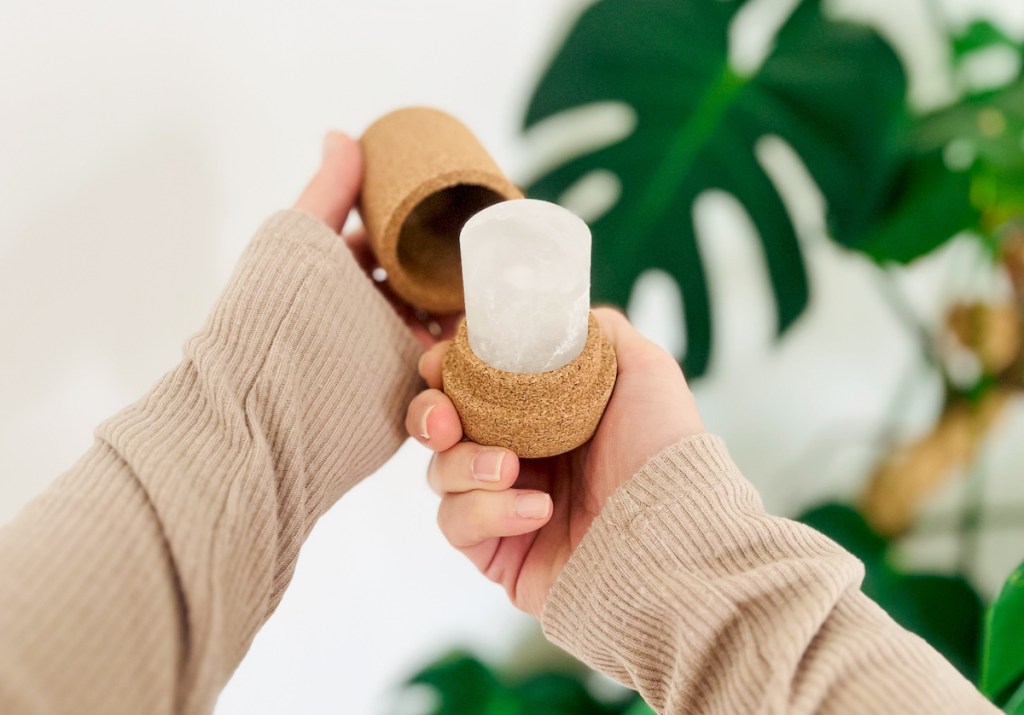 Hand holding a stick of crystal deodorant in cork container 