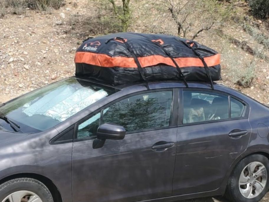 A car with a black and orange cargo bag on top