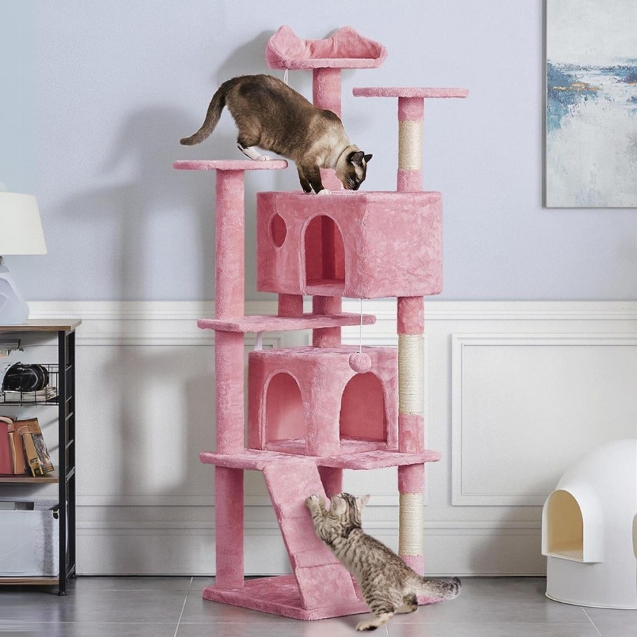 a light pink grey tall cat tower with cats in it and climbing on it in a living room