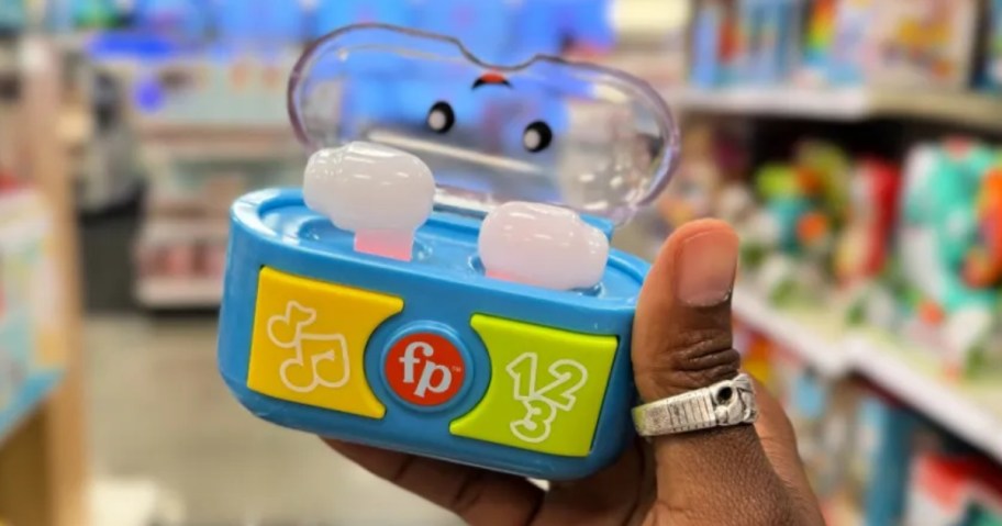 hand holding a blue, green, yellow, red, and white kid's toy earbud set in a store aisle