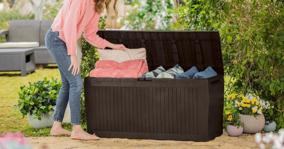 A woman placing pillows in a Keter Comfy 71 Gallon Resin Deck Box