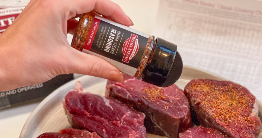 Woman sprinkling, Omaha steaks seasoning on rare pieces of steak