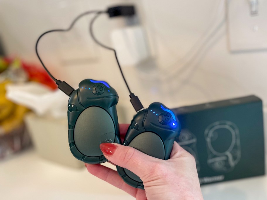 hand holding two Rechargeable Hand Warmers plugged into wall outlet