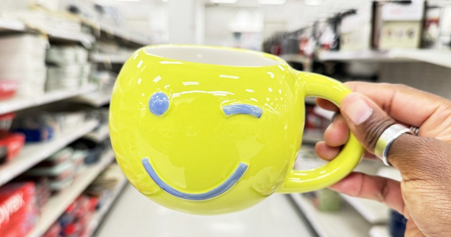 hand holding up a yellow winking face coffee mug