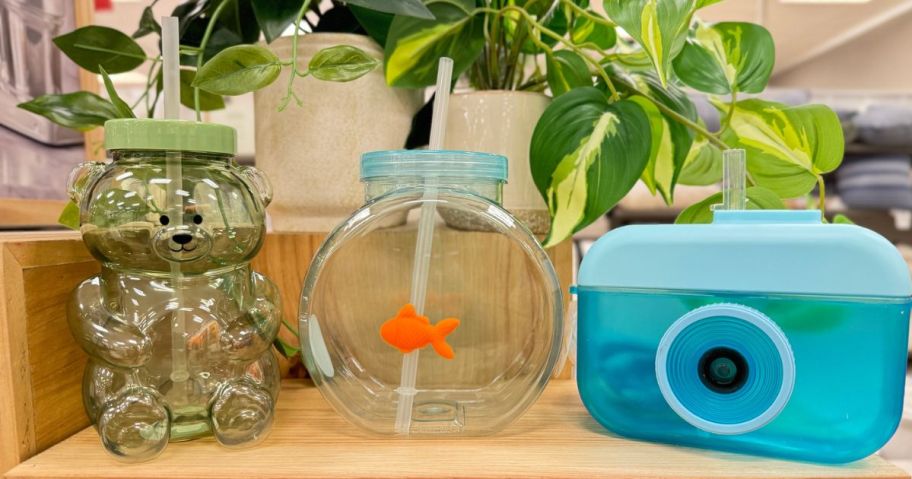 three styles of fun drinking cups with straws on counter - camera, fishbowl, and bear