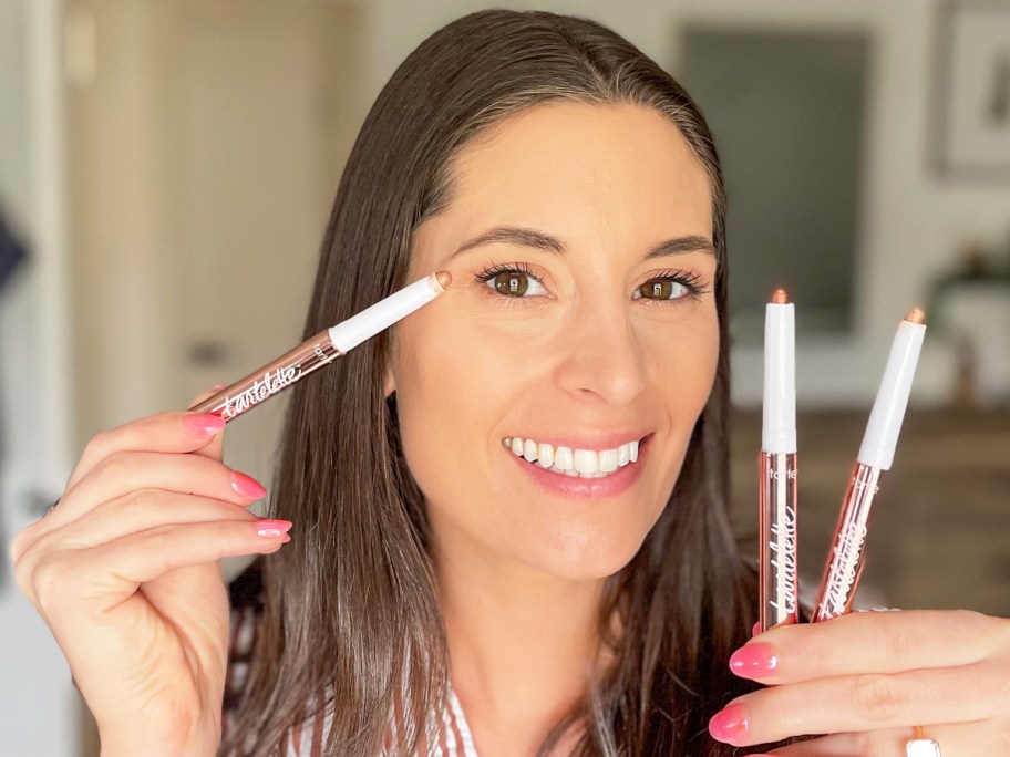 woman holding up three eyeshadow sticks near her face