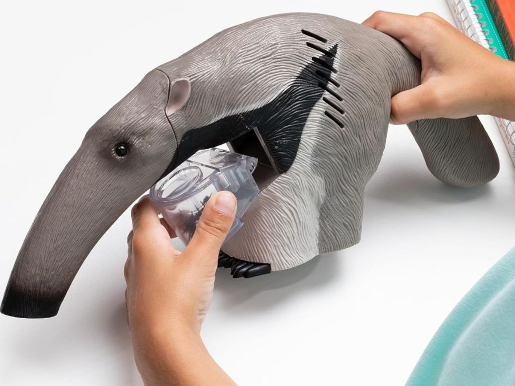 Child's hand removing the plastic container of live ants from an Uncle Milton Ant Vacuum