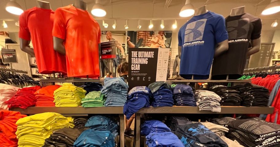 A display of folded men's t-shirts at the Under Armour store with mannequins wearing some styles