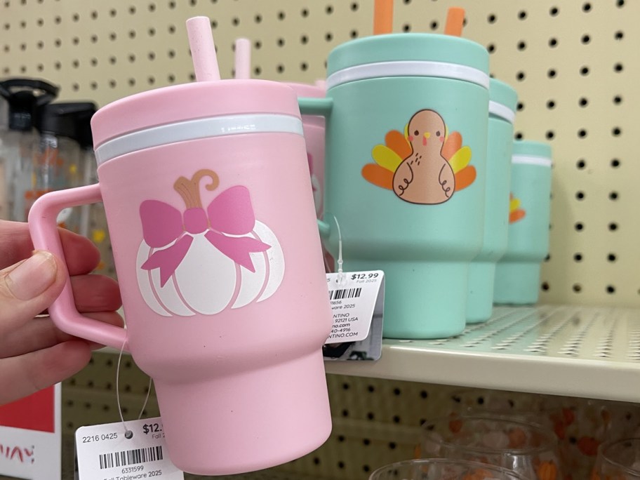 Woman holding the pumpkin and bow tumbler with the turkey version on the shelf behind it