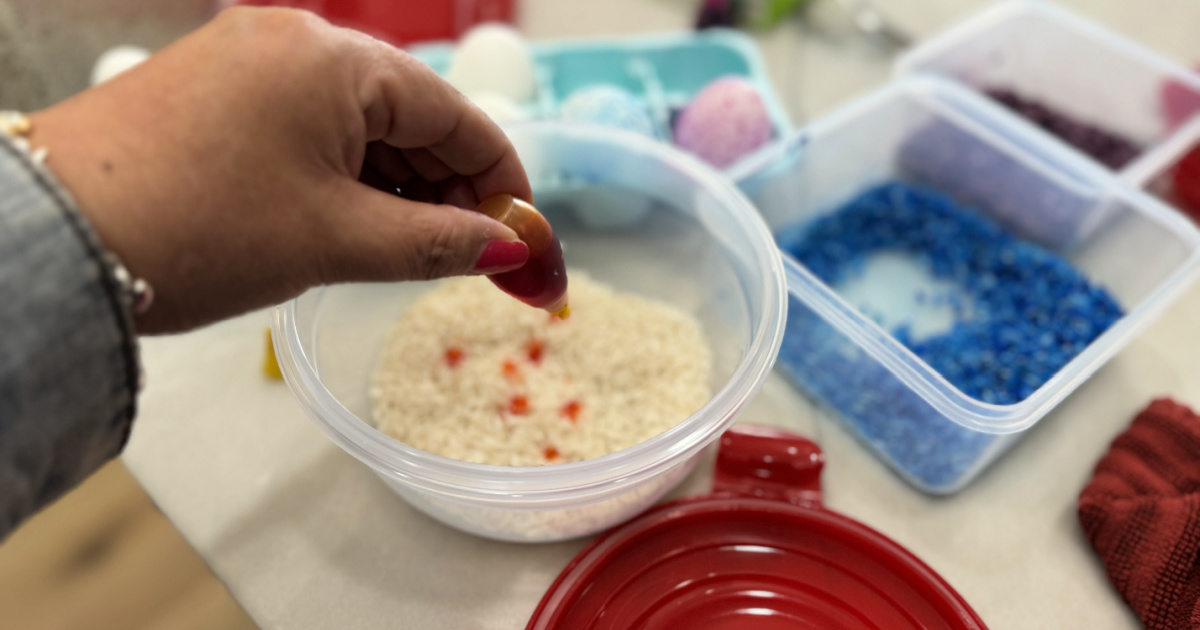 adding drops of yellow food coloring to plastic container with rice inside