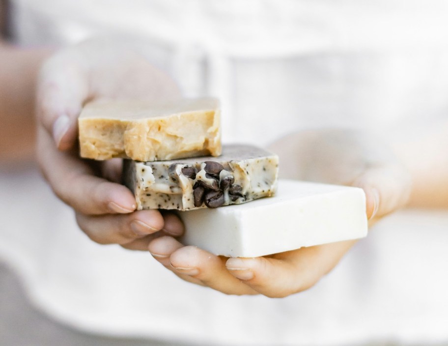 hands holding yellow brown and white bars of soap