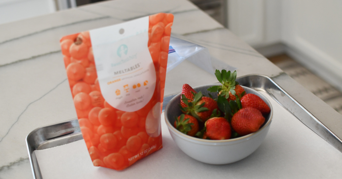 bowl of strawberries next to orange candy melts on a baking sheet pan