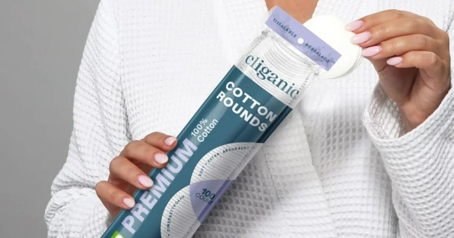 woman holding pack of cliganic organic cotton rounds while wearing a bathrobe