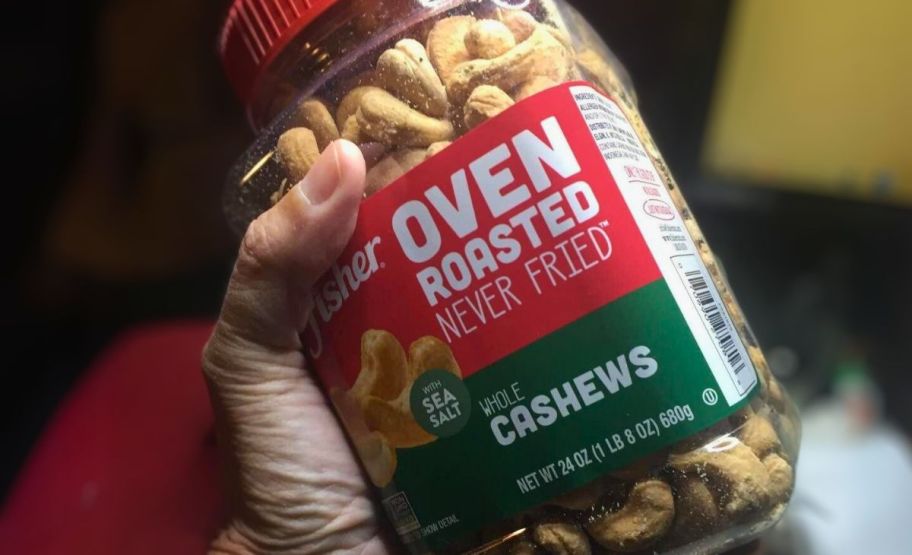 a man's hand displaying a plastic jar of cashews