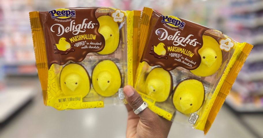 a woman's hand holding two packages of peep chocolate dipped smores