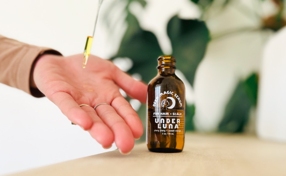 hand dropping oil on palm with amber glass bottle on wood table