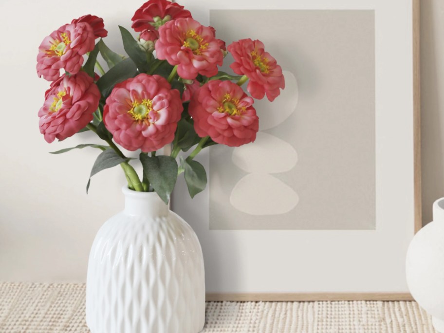 Pink coral zinnia flowers in white vase on mantle