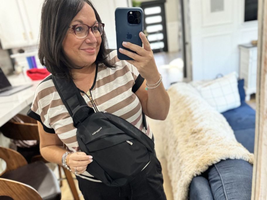 Woman taking a picture of herself in a mirror while wearing a Baggallini sling bag