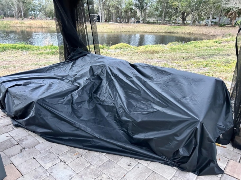 black patio furniture cover over patio furniture on a patio, backyard behind it