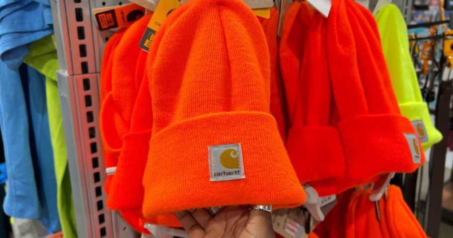 Hand touching a bright orange Carhartt beanie hanging on a display at a Carhartt Store