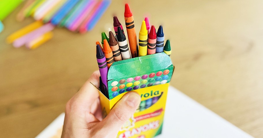 hand holding an open box of crayons