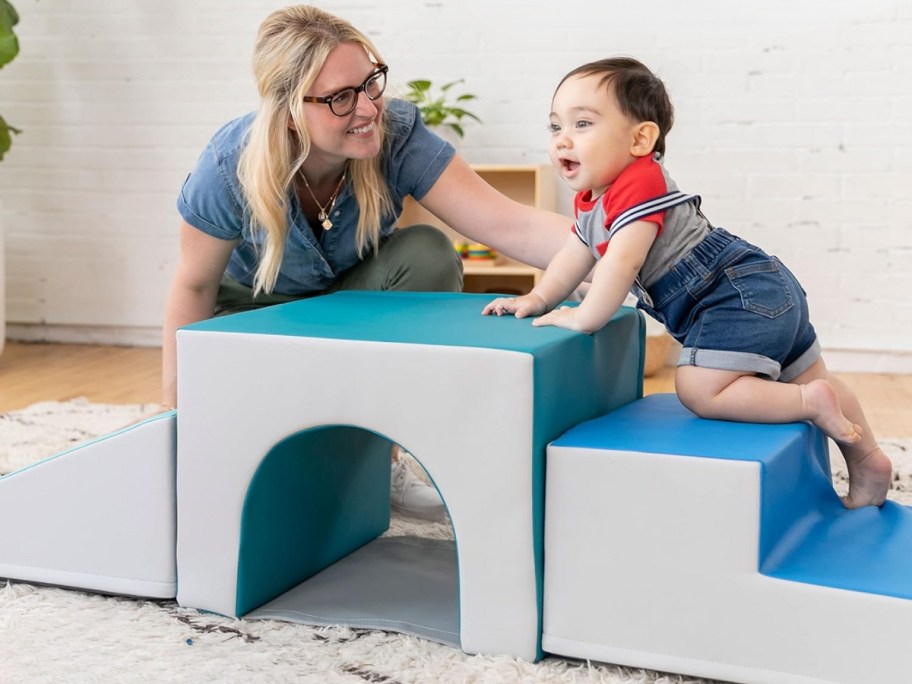 mom watching a baby climb on a soft playset in a living room