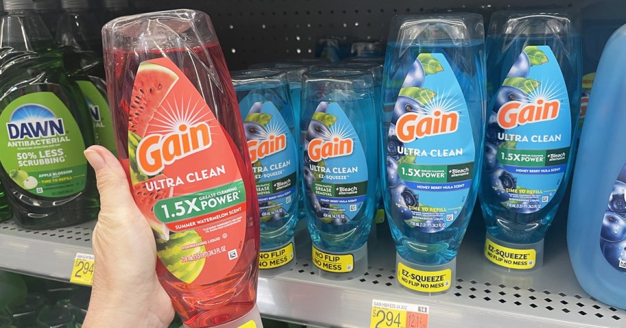 hand holding bottle of Gain EZ-Squeeze Dish Soap in front of shelf with more bottles