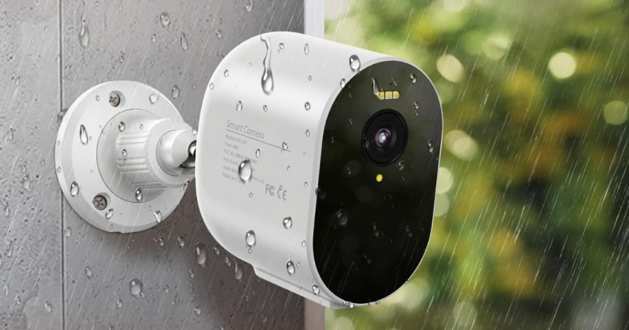 white TENVIS brand Security Camera attached to an exterior wall with rain coming down around it